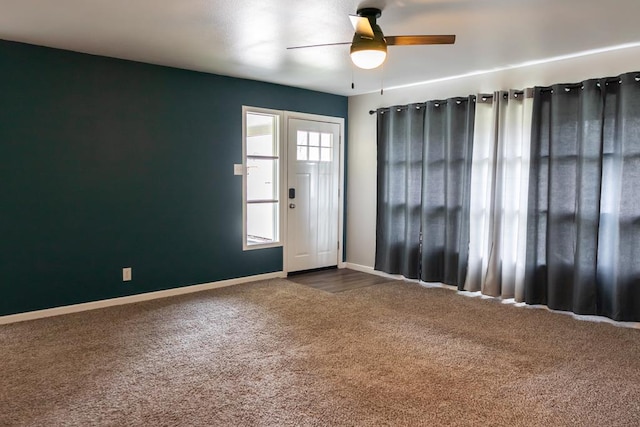 empty room with baseboards, dark colored carpet, and ceiling fan