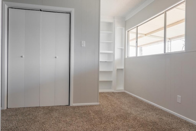 unfurnished bedroom with a closet, wood walls, ornamental molding, and carpet floors