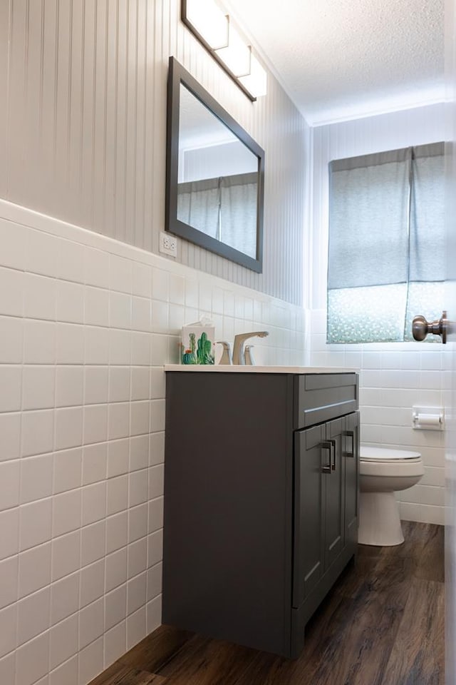 bathroom featuring vanity, wood finished floors, a textured ceiling, tile walls, and toilet