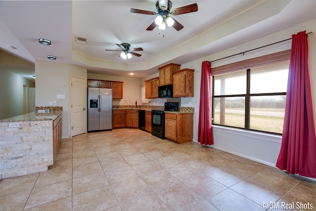 kitchen with brown cabinets, black appliances, a raised ceiling, and light stone countertops