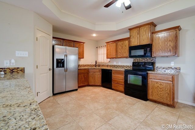 kitchen featuring a tray ceiling, brown cabinetry, ornamental molding, a sink, and black appliances