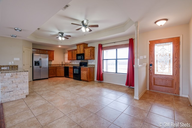 kitchen featuring black appliances, a tray ceiling, light stone counters, and brown cabinets