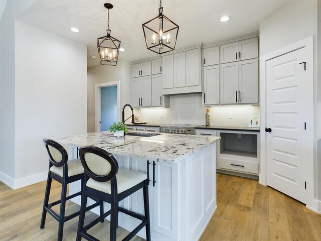 kitchen with hanging light fixtures, sink, a center island with sink, and light stone counters