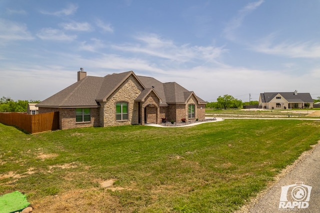 french country inspired facade with a front lawn, fence, stone siding, and a chimney