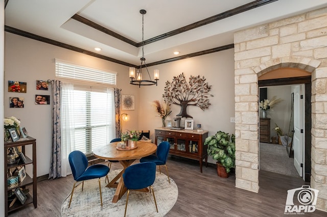 dining area featuring crown molding, a raised ceiling, ornate columns, wood finished floors, and a notable chandelier