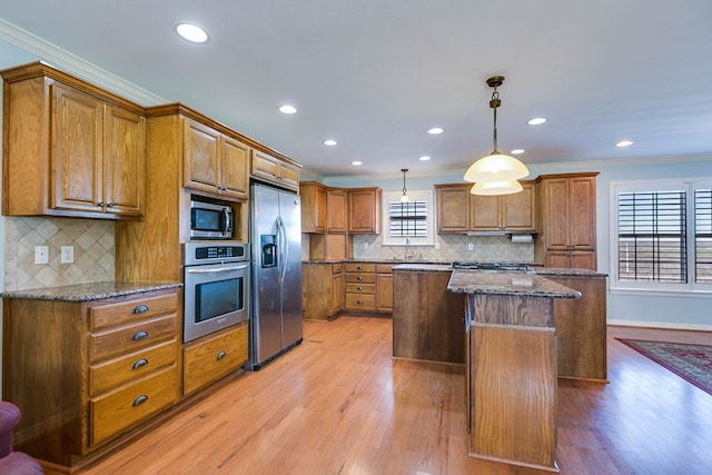 kitchen featuring a kitchen island, ornamental molding, appliances with stainless steel finishes, and decorative light fixtures