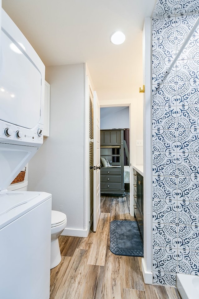 bathroom featuring hardwood / wood-style flooring, stacked washer and clothes dryer, and toilet