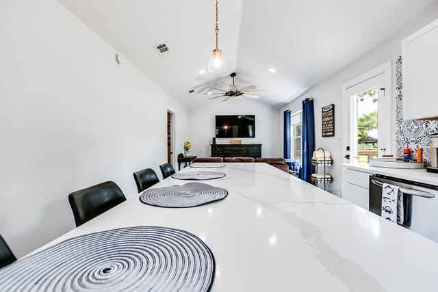 kitchen with light stone countertops, white cabinets, a kitchen bar, decorative light fixtures, and vaulted ceiling