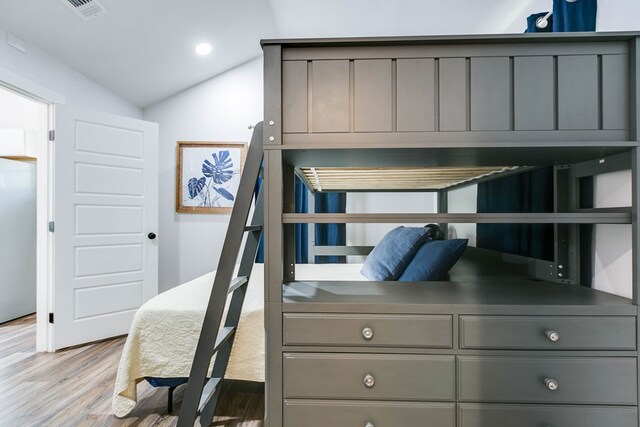 bedroom with stainless steel fridge, light hardwood / wood-style floors, and vaulted ceiling