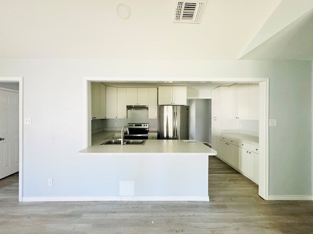 kitchen with sink, white cabinetry, vaulted ceiling, appliances with stainless steel finishes, and light hardwood / wood-style floors