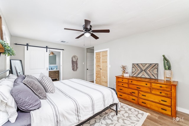 bedroom with ceiling fan, ensuite bath, a barn door, and light hardwood / wood-style floors