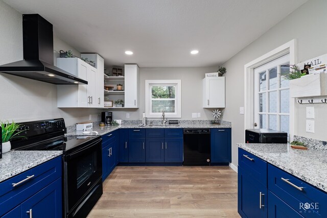 kitchen with white cabinets, black appliances, blue cabinetry, wall chimney range hood, and light wood-type flooring