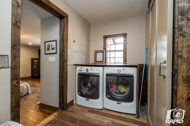 clothes washing area with washer and clothes dryer, electric panel, a barn door, and wood-type flooring