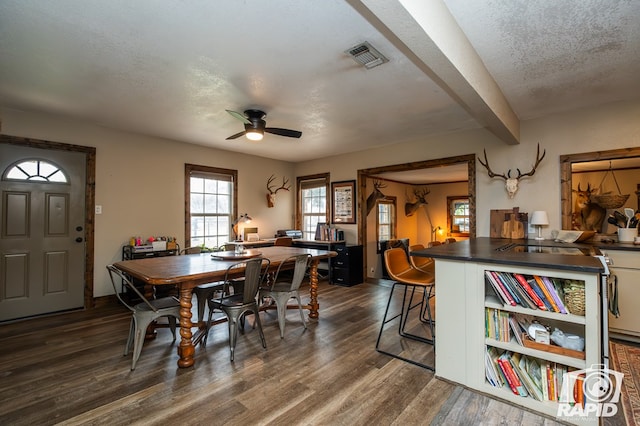 dining room with ceiling fan, dark wood-type flooring, a textured ceiling, and beam ceiling