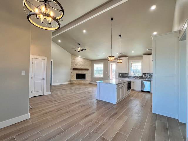 kitchen with a stone fireplace, dishwasher, white cabinets, hanging light fixtures, and a center island