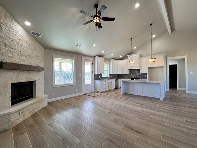 kitchen with light hardwood / wood-style flooring, hanging light fixtures, dishwasher, a kitchen island, and white cabinets