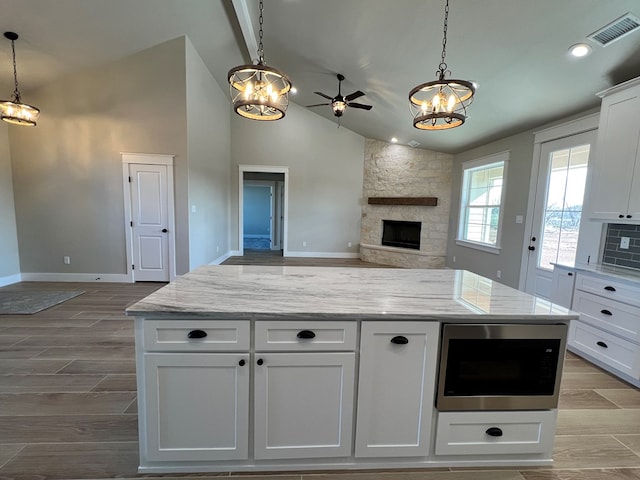 kitchen with hanging light fixtures, stainless steel microwave, white cabinets, and light stone counters