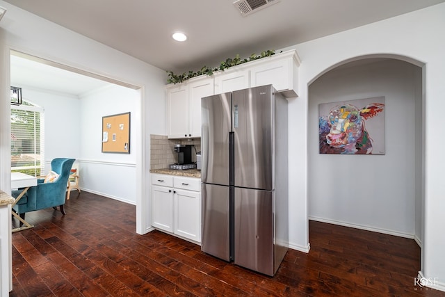 kitchen with dark wood-type flooring, light stone counters, stainless steel refrigerator, white cabinets, and backsplash