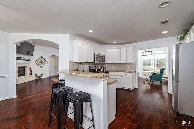 kitchen featuring dark hardwood / wood-style floors, kitchen peninsula, white cabinets, stainless steel appliances, and backsplash