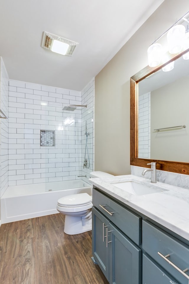 full bathroom featuring vanity, hardwood / wood-style floors, tiled shower / bath combo, and toilet