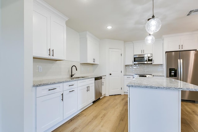 kitchen with visible vents, a kitchen island, a sink, appliances with stainless steel finishes, and light wood-type flooring