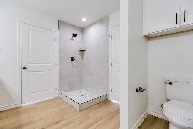 bathroom featuring baseboards, toilet, wood finished floors, and a tile shower