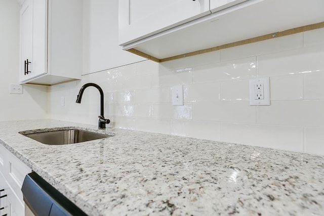 kitchen with light stone counters, decorative backsplash, white cabinets, and a sink