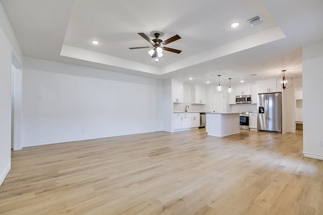 unfurnished living room with visible vents, baseboards, a tray ceiling, ceiling fan with notable chandelier, and light wood-style flooring