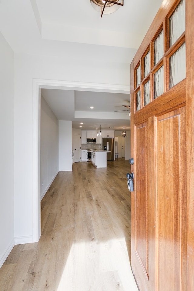 foyer entrance featuring a ceiling fan, a raised ceiling, light wood-style floors, and baseboards