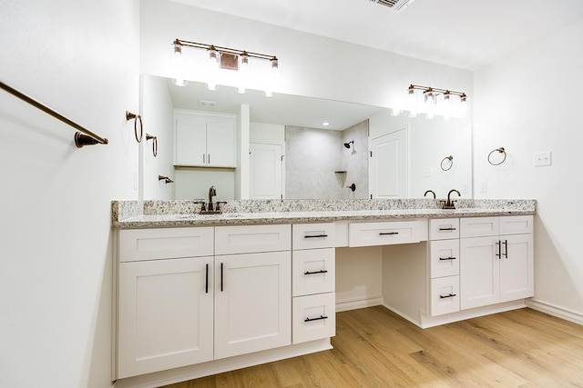 bathroom featuring double vanity, tiled shower, wood finished floors, and a sink