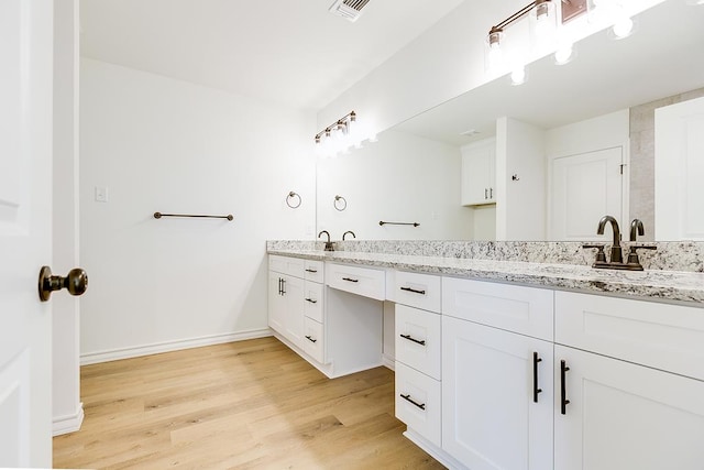 bathroom with wood finished floors, visible vents, baseboards, double vanity, and a sink