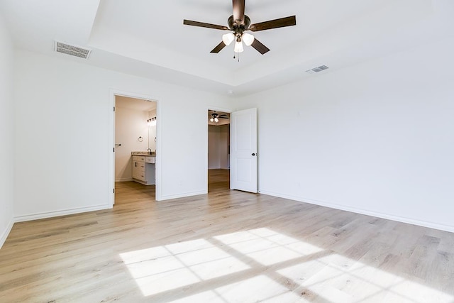 unfurnished bedroom with a raised ceiling, light wood-style flooring, baseboards, and visible vents