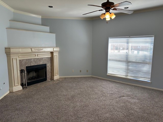 unfurnished living room with a tiled fireplace, crown molding, and carpet flooring