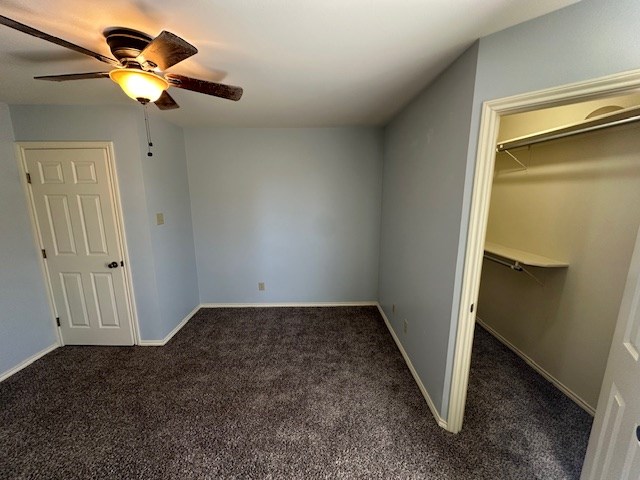 unfurnished bedroom with dark colored carpet, ceiling fan, and a closet