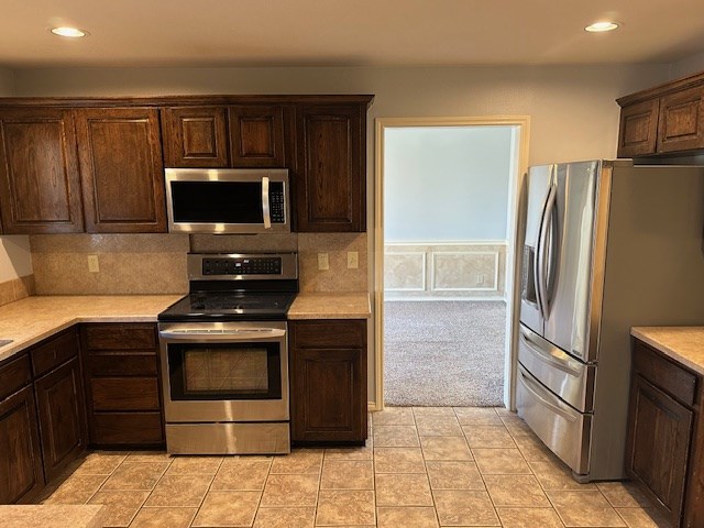 kitchen with stainless steel appliances, tasteful backsplash, dark brown cabinets, and light colored carpet