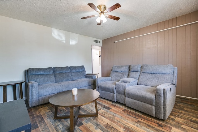 living room with dark wood-type flooring, ceiling fan, wooden walls, and a textured ceiling