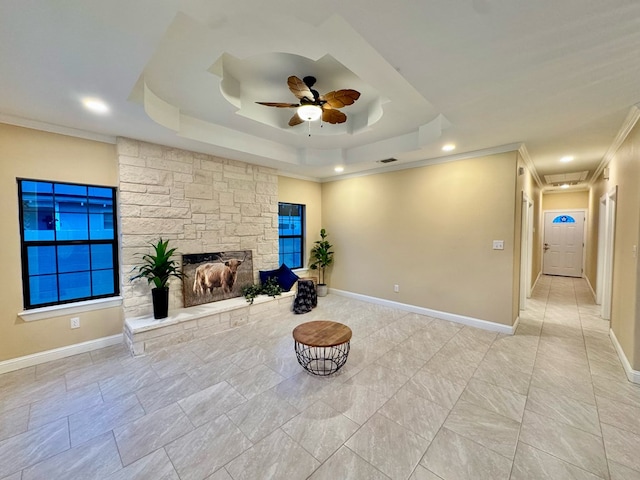 unfurnished room with crown molding, ceiling fan, a tray ceiling, and a stone fireplace