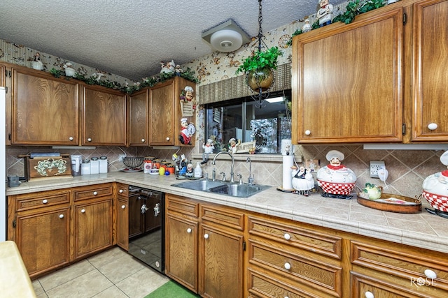 kitchen featuring light tile patterned flooring, dishwasher, sink, tile counters, and a textured ceiling