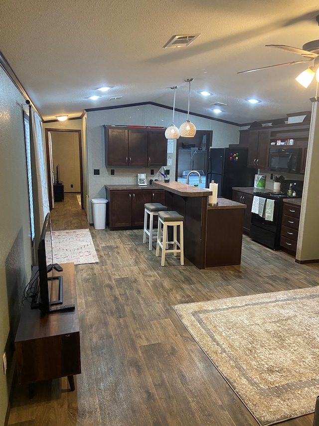 kitchen featuring lofted ceiling, pendant lighting, black appliances, an island with sink, and a kitchen bar