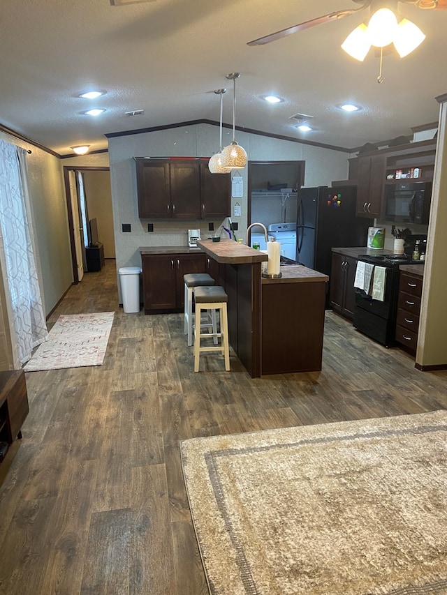 kitchen featuring lofted ceiling, hanging light fixtures, dark brown cabinets, black appliances, and a center island with sink