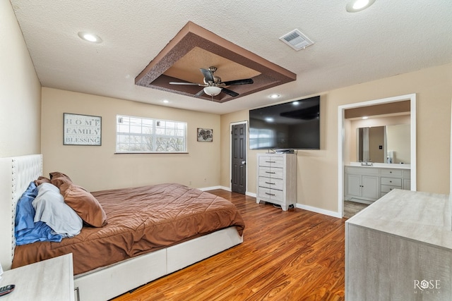 307 E 12th St, Big Lake, TX 76932 - bedroom featuring baseboards, a textured ceiling, a raised ceiling, ensuite bath, and wood finished floors