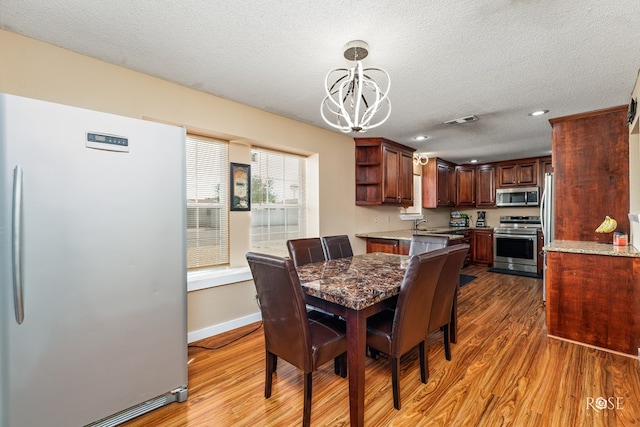 307 E 12th St, Big Lake, TX 76932 - dining area with baseboards, a chandelier, a textured ceiling, visible vents, and wood finished floors