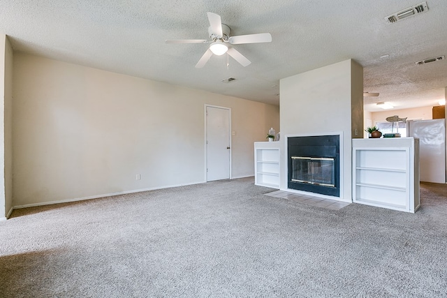 1826 High Butte Dr, San Angelo, TX 76905 - unfurnished living room featuring carpet floors, a ceiling fan, a textured ceiling, a fireplace with flush hearth, and baseboards