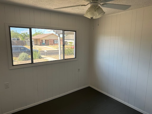 spare room featuring ceiling fan, a textured ceiling, and wood walls