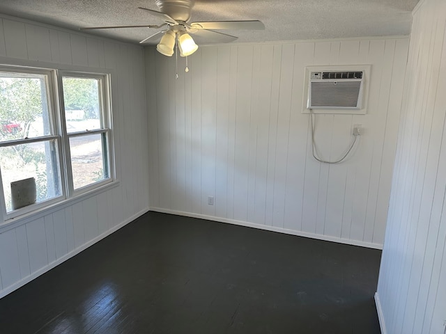 empty room with dark hardwood / wood-style floors, wooden walls, a wall unit AC, ceiling fan, and a textured ceiling