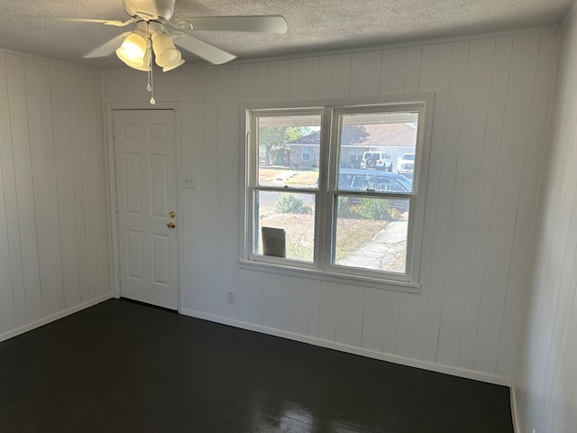 empty room with ceiling fan, dark wood-type flooring, and a textured ceiling