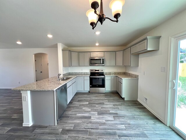 kitchen featuring stainless steel appliances, gray cabinets, kitchen peninsula, and light stone countertops