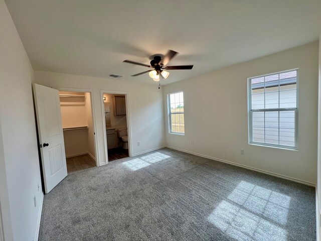 unfurnished bedroom featuring ensuite bath, a spacious closet, carpet flooring, a closet, and ceiling fan