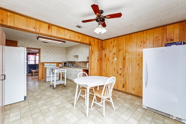 kitchen with ceiling fan, white appliances, wooden walls, and white cabinets