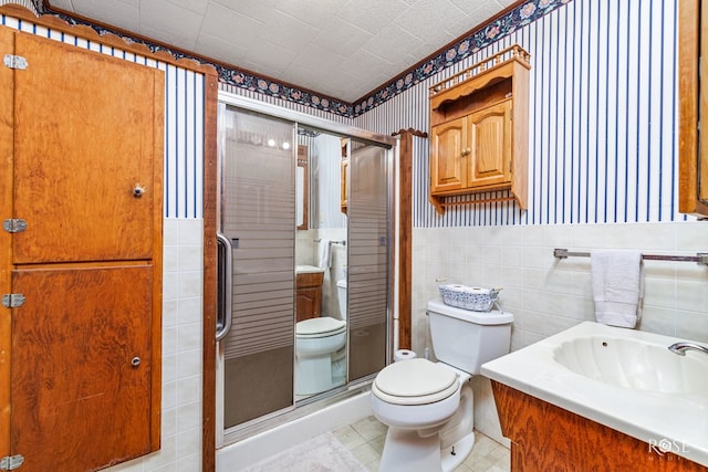 bathroom with vanity, a shower with shower door, tile walls, and toilet